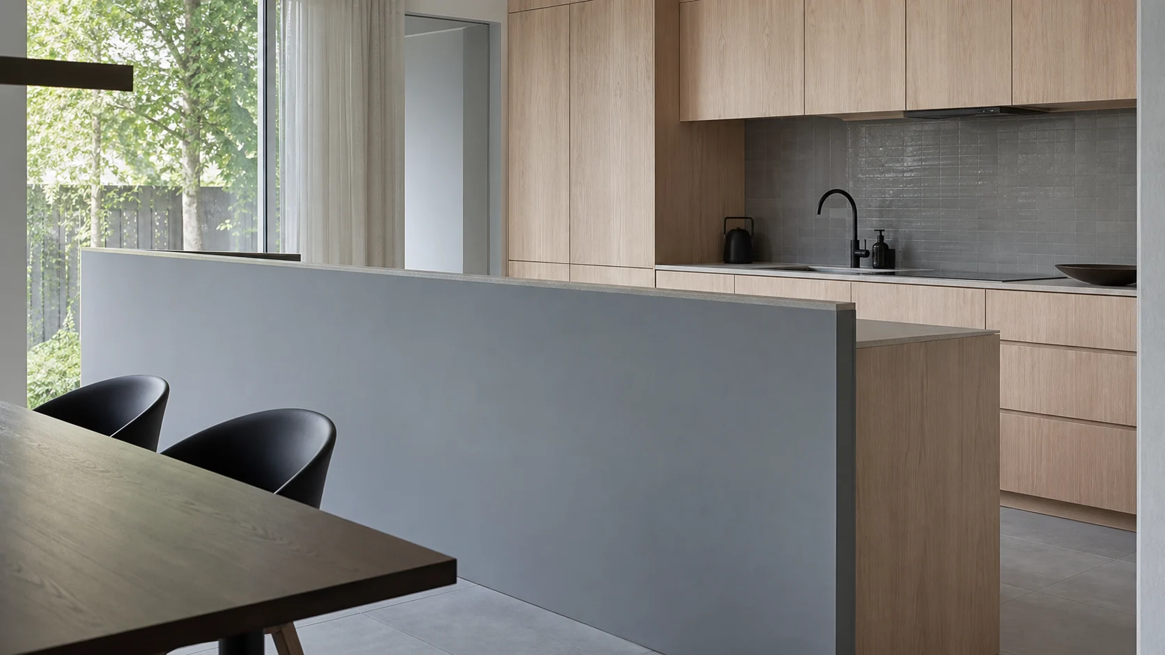 ダイニング側から座った目線で見たキッチンの腰壁。拭き取れる寒色のマットな面が、石のワークトップと淡いオークの収納に対する高さの関係を見せる