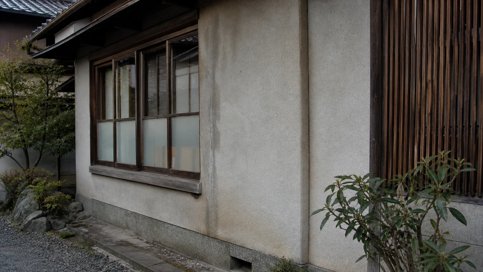 経年した住宅外壁の染みと細い亀裂を斜光の下で観察する様子